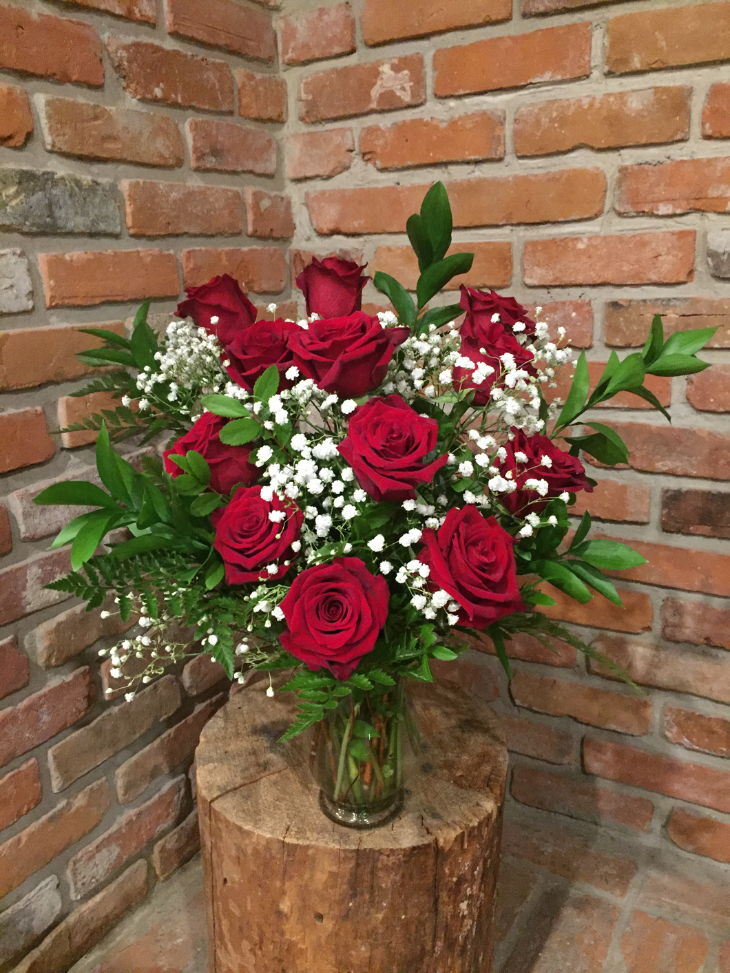 A vase arrangement of a dozen of our premium Explorer Red Roses with fragrant white babies breath and an assortment of foliages